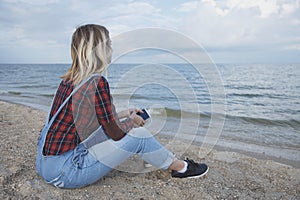 Beautiful blonde girl sits on the beach and looks at the sea