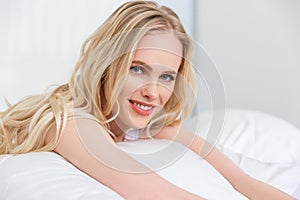 beautiful blonde girl smiling at camera while lying in bed