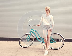 Beautiful blonde girl is standing near the vintage bicycle have fun and good mood looking in camera and smiling, warm, tonning