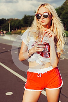 Beautiful blonde girl in vintage red shorts and white T-shirt holds a hand a glass of fresh cool summer drink. summer vacatio