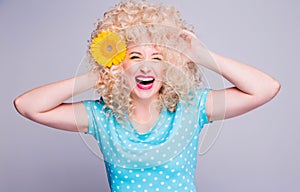 Beautiful blonde girl with voluminous curly hairstyle, in a blue polka dot blouse and with a flower of a sunflower in her hair on