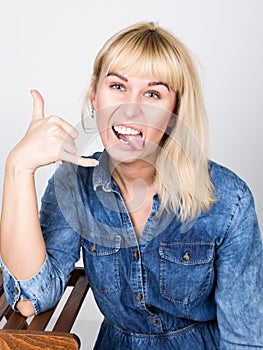 Beautiful blonde girl wearing a denim shirt showing tongue and fingers makes Shaka sign