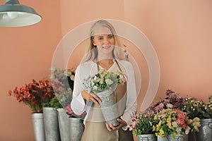 Beautiful blonde hair girl standing with confidence in front of flower in open retails flora shop. Small business owner concept photo