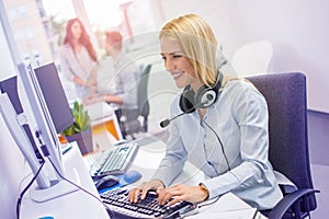 Beautiful blonde haired female helpline operator using computer at office.