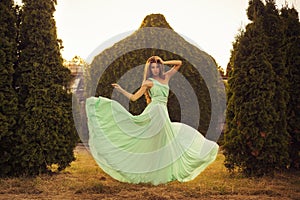 Beautiful blonde with a long curly hair in a long evening dress in motion outdoors near retro vintage building in summer sunset