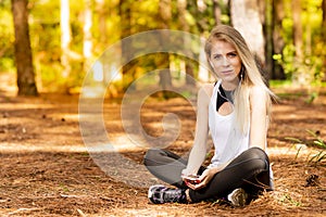 Beautiful blonde model in the middle of pines sitting using cellphone with headset. Listening to music