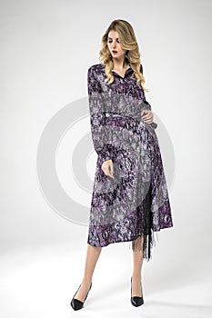 Beautiful blonde model posing in long sleeve, long chic purple dress