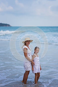 Beautiful blonde mother lady in white dress with her pretty little daughter in white dress at the seaside. Happy family on the