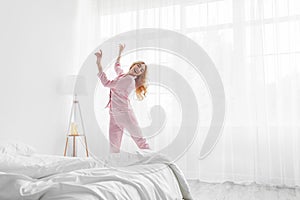 Beautiful blonde in pajama waking up in morning, happy young lady greets new day with good mood