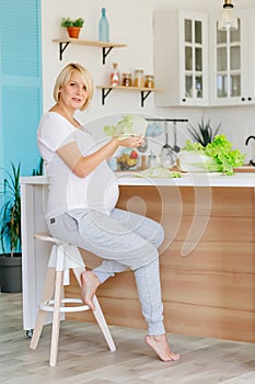 A beautiful blonde pregnant blonde in the Scandinavian-style kitchen at the table parses green cabbage.