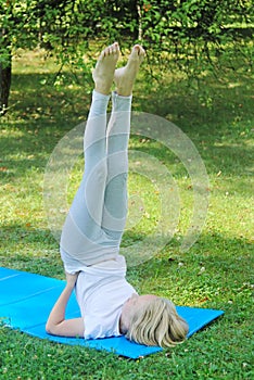 Beautiful blonde preteen girl in light clothing practicing yoga on a mat. Healthy lifestyle. Outdoors workout.