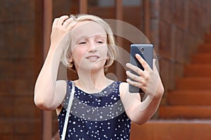 Beautiful blonde preteen girl using a phone, makes the photo a front camera, taking a self portrait with mobile phone.