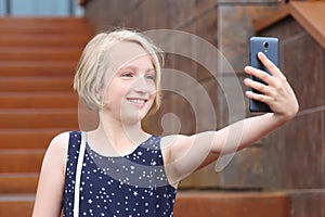 Beautiful blonde preteen girl using a phone, taking a self portrait with mobile phone