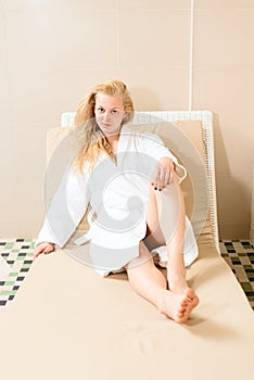 Beautiful blonde is relaxing in spa salon. charming young girl lying in a white robe on the sofa.