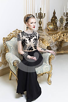 Beautiful blonde royal woman laying on a retro sofa in gorgeous luxury dress