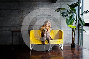 Beautiful blonde sitting on yellow couch. Moving house concept. Choosing furniture. Hesitation notion