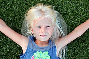 Beautiful blonde smiling girl lying on the grass on a summer day