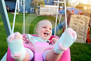 Beautiful blonde smiling girl is swinging outside on a summer day