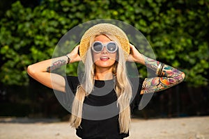 Beautiful blonde is smiling and looking at the morning sea. Holds a hat with his hands with tattoos. Travel to Thailand. photo