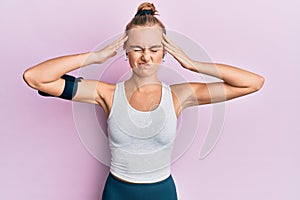 Beautiful blonde sport woman wearing arm band and earphones with hand on head, headache because stress