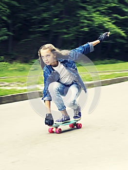 Beautiful blonde teen girl in jeans shirt, on skateboard in park