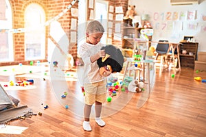 Beautiful blonde toddler playing with monkey mask standing around lots of toys at kindergarten