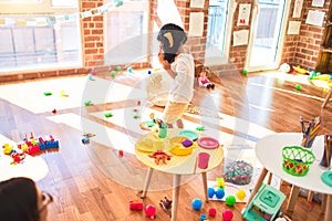 Beautiful blonde toddler playing with monkey mask standing around lots of toys at kindergarten