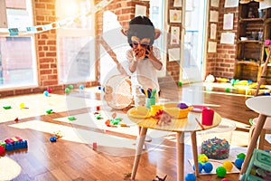 Beautiful blonde toddler playing with monkey mask standing around lots of toys at kindergarten