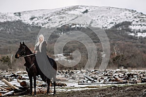 Beautiful blonde Viking in a black cape on horseback