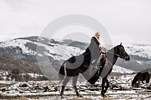 Beautiful blonde Viking in a black cape on horseback