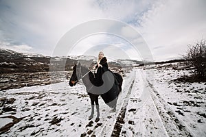 Beautiful blonde Viking in a black cape on horseback