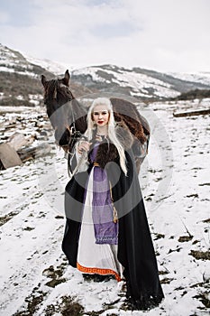 Beautiful blonde Viking in a black cape on horseback