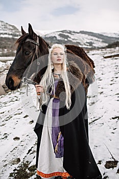 Beautiful blonde Viking in a black cape on horseback