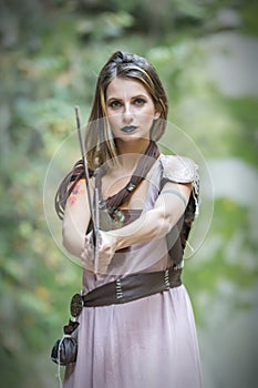 Beautiful blonde viking woman with a shield and a sword near a waterfall