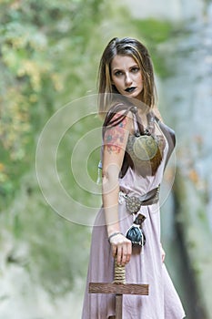 Beautiful blonde viking woman with a shield and a sword near a waterfall