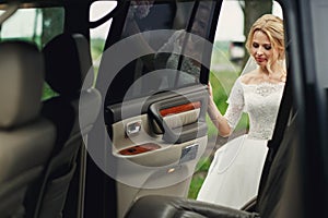 Beautiful blonde wedding bride in white dress getting into elegant car