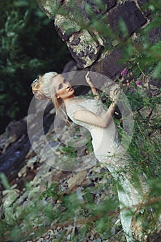 Beautiful blonde in a wedding dress on the nature near the rocks