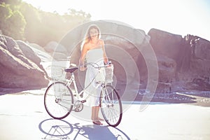 Beautiful blonde in white sundress standing with bike on the beach