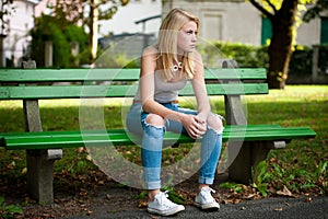 Beautiful blonde woamn rests on a bench in park