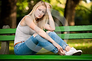 Beautiful blonde woamn rests on a bench in park