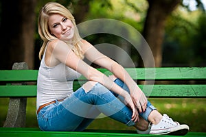 Beautiful blonde woamn rests on a bench in park