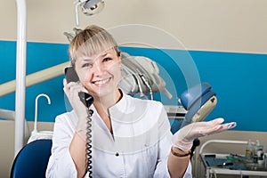 Beautiful blonde woman administrator at the dental clinic holding the phone, records of patients at the reception