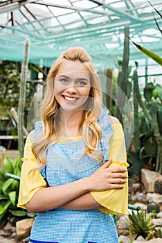 beautiful blonde woman in apron standing with crossed arms and smiling at camera