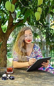 Beautiful blonde woman artist and illustrator drawing, sitting by the table with electronical tablet and stylus