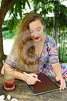 Beautiful blonde woman artist and illustrator drawing, sitting by the table with electronical tablet and stylus