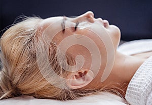 Beautiful blonde woman in bathrobe is lying with silicone patches under her eyes in spa salon or clinic