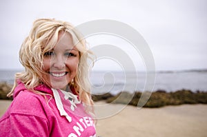 Beautiful blonde woman with beach waves and touseled hair stands and poses on a windy beach along the Pacific Coast Highway in