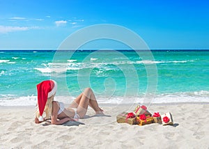 Beautiful blonde woman in bikini, red christmas hat and gift box