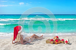 Beautiful blonde woman in bikini, red christmas hat and gift box