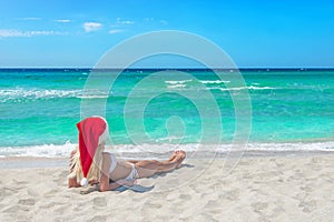 Beautiful blonde woman in bikini and red christmas hat on sea be